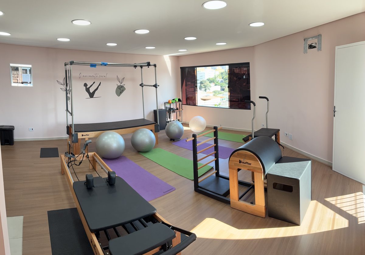 Sala de pilates iluminada por janelas amplas, com aparelhos e tatames